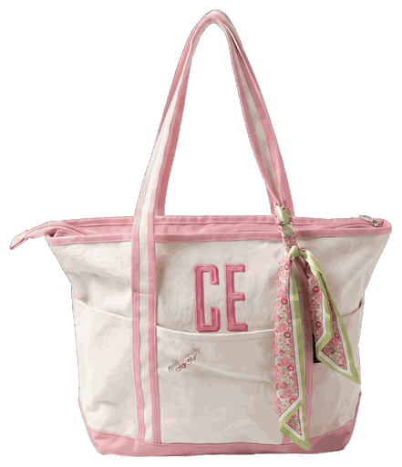 A cream tote with pink trim and a two-letter monogram on the front, and a scarf tied to one handle